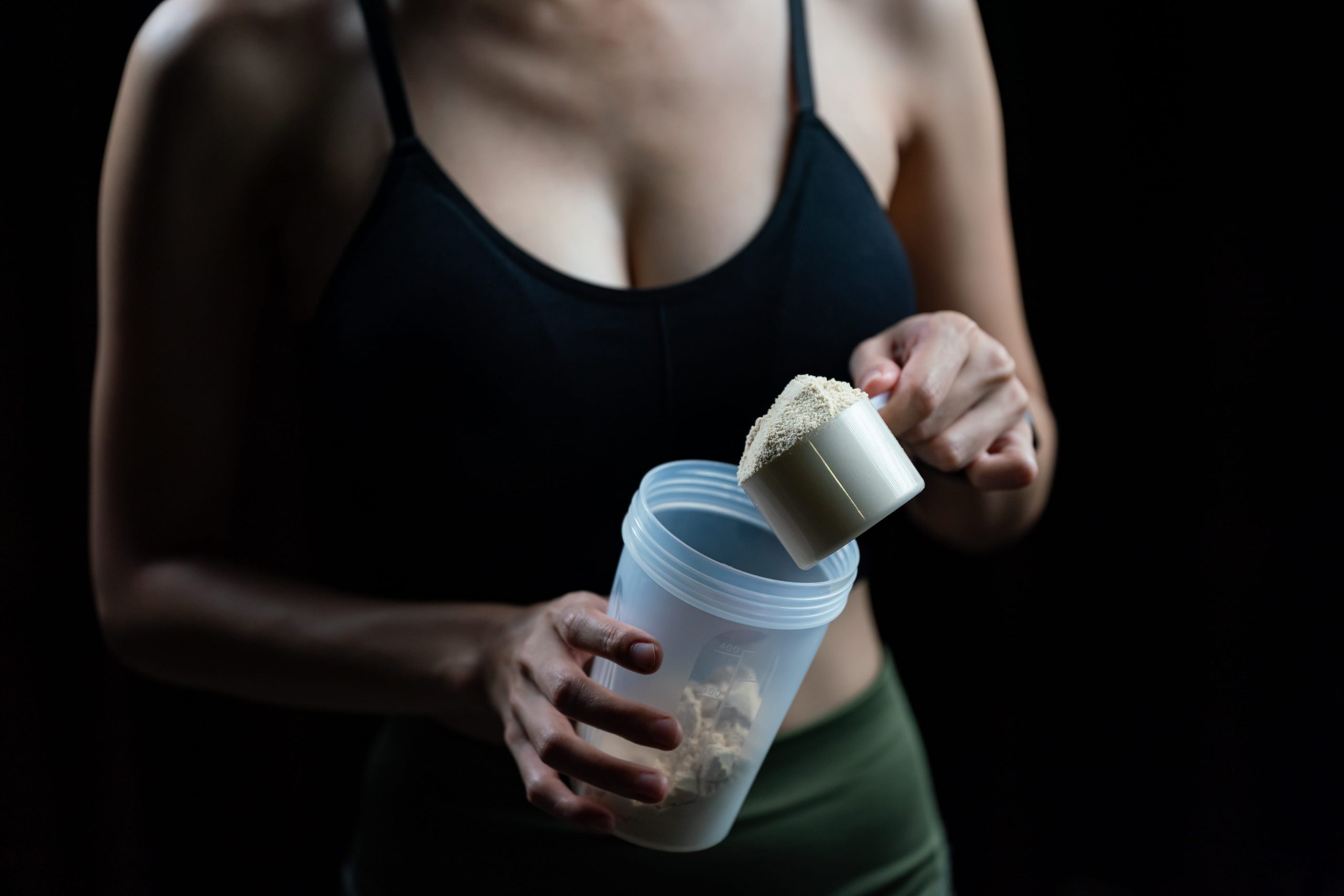 A woman in sport attires holding a shaker bottle and a scoop of Phytae plant-based protein.